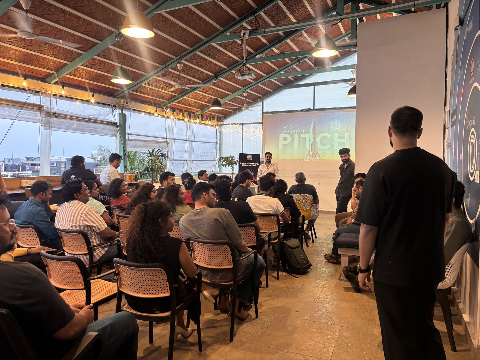 A full house at a past Founders Pitch:
            rows of seated founders turned toward the screen, with the Founders Pitch title slide
            projected behind the speakers.